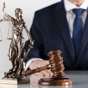 What Does Blind Justice Mean? photo of man in business suit with blindfolded Lady Justice holding scales and sword next to gavel on table