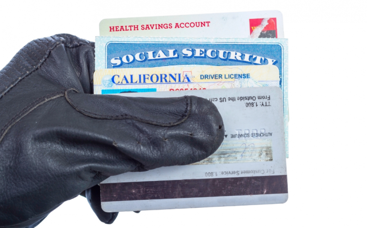 What You Need to Know if You've Been Charged with Identity Theft - gloved hand holding various identity cards, specifically a health savings account id card, social security card, California drivers license, and credit card