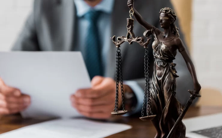 What Does it Mean to Take the Law Into Your Own Hands? scales of justice figurine on table with man holding a document in the background