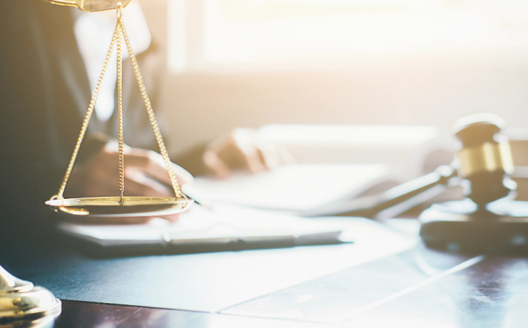 What Does Get Off on a Technicality Mean? - scales and judge gavel on desk with lawyer reviewing case documents in background