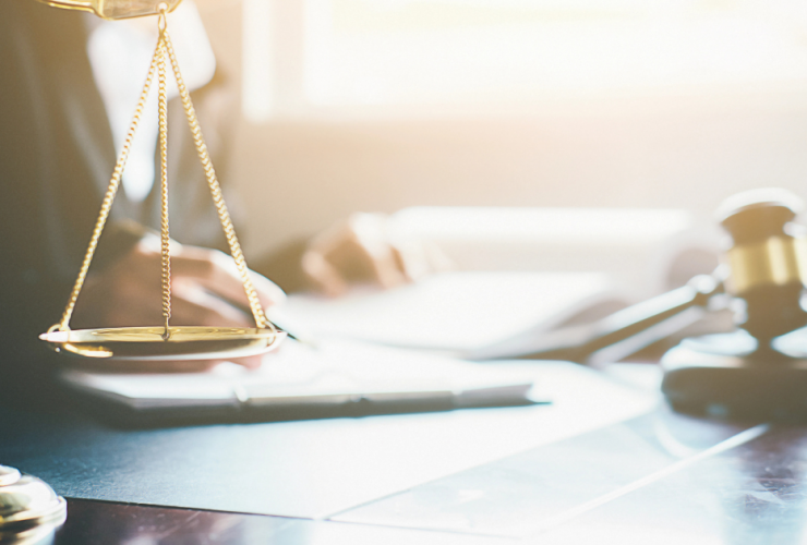 What Does Get Off on a Technicality Mean? - scales and judge gavel on desk with lawyer reviewing case documents in background