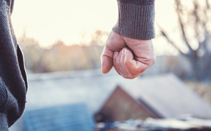 closeup of a man in a hoodie clenching fist in anger from behind